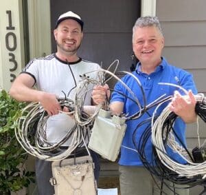 2 men hold telecom wires and a service box that Wire Free Sky removed from their home