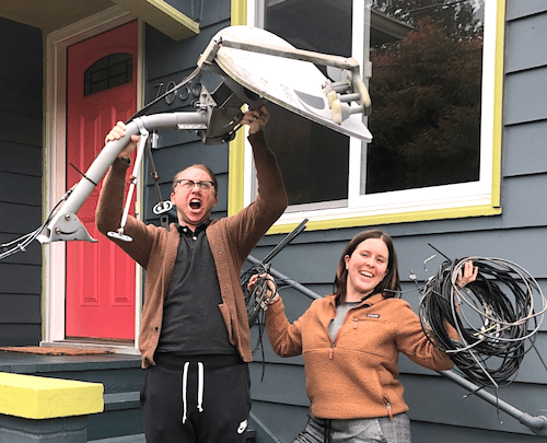 a man and women victoriously hold a satellite dish above their heads and its wires