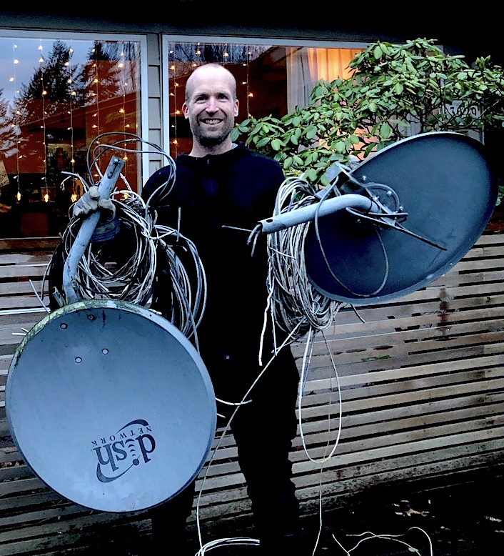 Man in front of house holding 2 Satellite dishes and coils of wire.