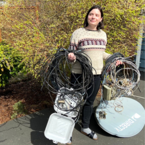 Photo of women with satellite dish, service box, and coils of telecom wire just removed from her home