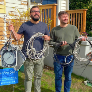 Photo of 2 satisfied men holding the telecom wire and service box removed from their home
