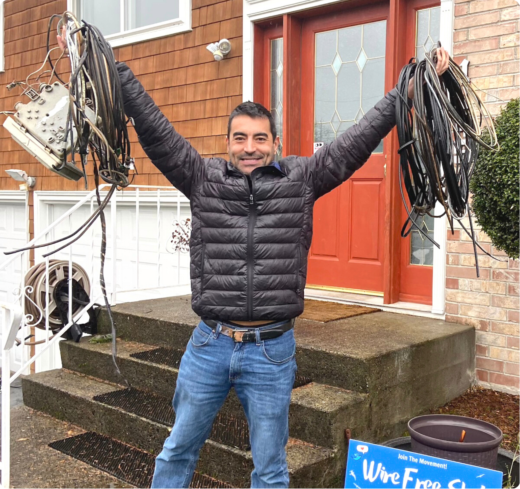 photo of man with raised arms and holding coils of wire and service box removed from his home